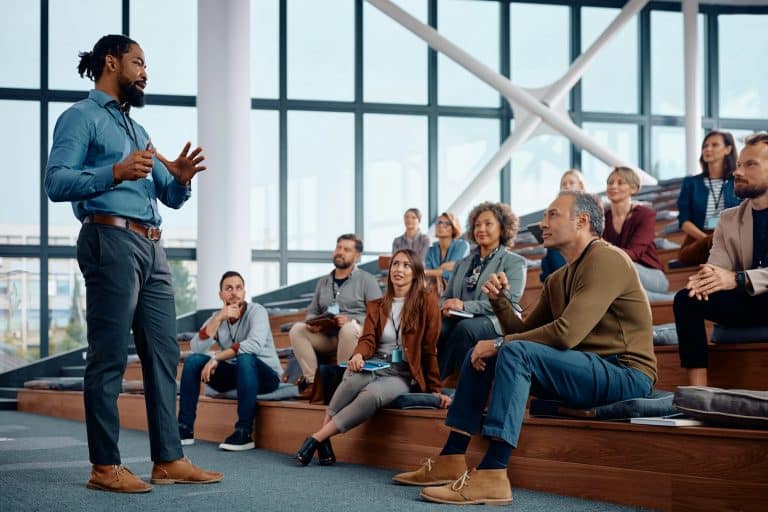 Black businessman talking to large group of entrepreneurs during education event in conference hall.