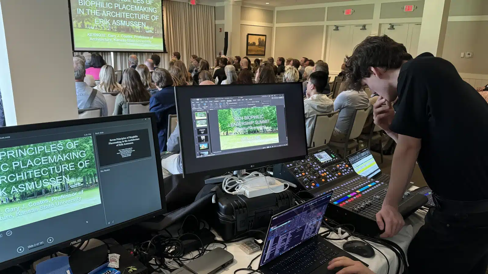 Event Maestro technician operating a digital sound mixer beside presentation monitors during a conference