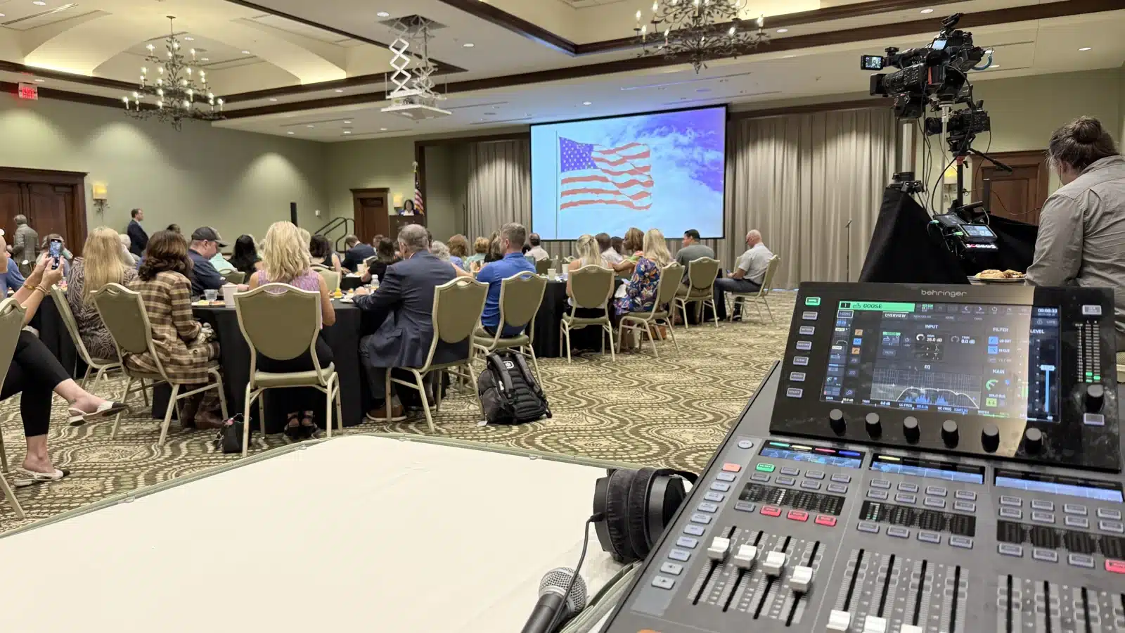 Sound mixing console, handheld microphone and video camera beside a conference audience and large projection screen
