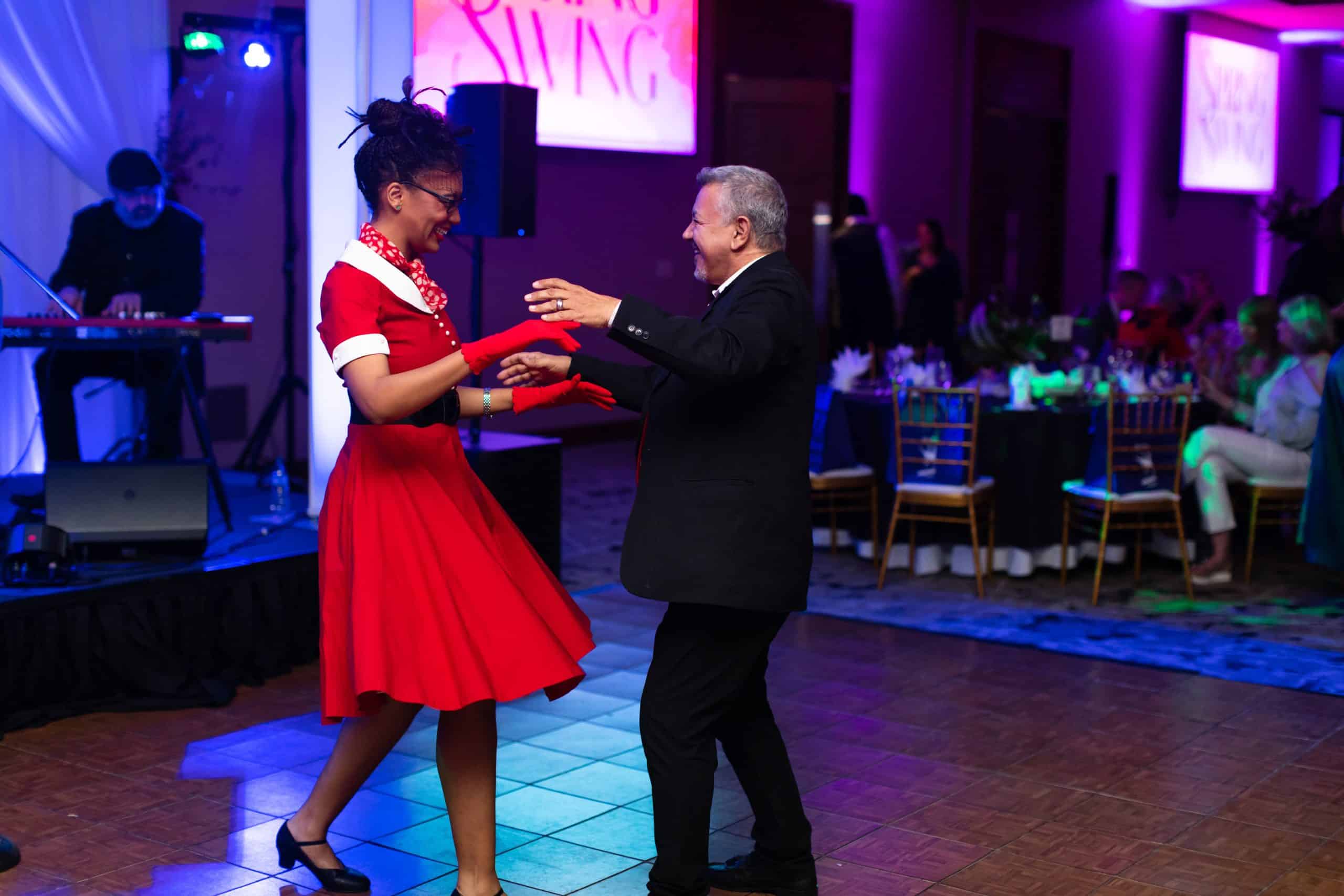Guests dance beside a live band stage with blue and purple lighting at Spring Swing Gala.